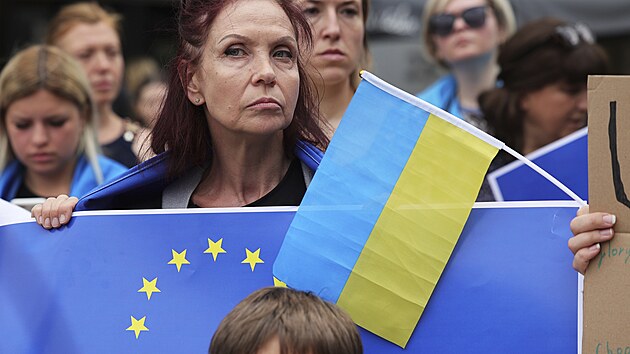 Lidé drží vlajky EU a Ukrajiny během shromáždění v Bruselu. (23. června 2022)