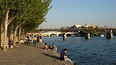 Lidé sedí u řeky Seiny v Paříži.