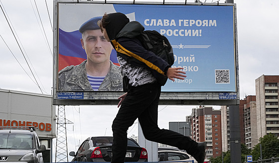 Chlapec v St. Petersburgu prochází pod billboardem s nápisem Sláva hrdinm...