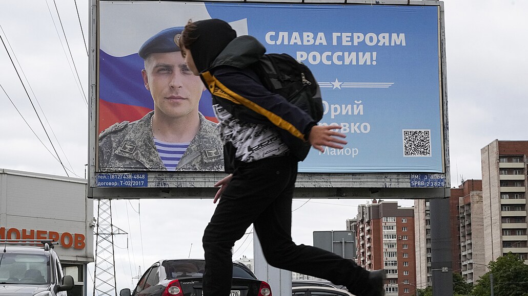 Chlapec v St. Petersburgu prochází pod billboardem s nápisem Sláva hrdinm...