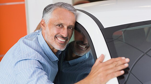 Smiling man hugging a white car at new car showroom