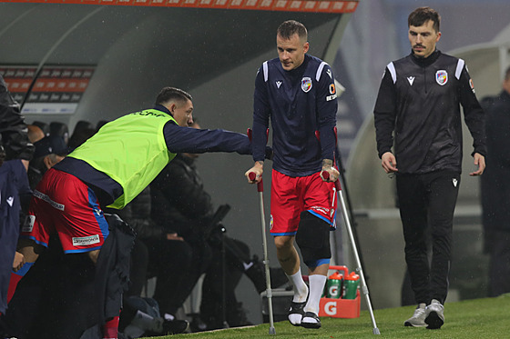 Zranný Jan Sýkora se vrací na laviku o berlích s obvázaným kolenem.