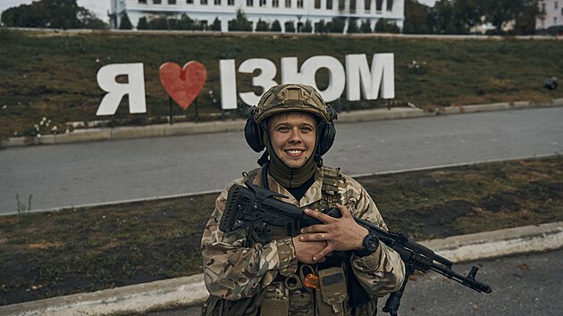 Voják ukrajinské armády se usmívá před nápisem v osvobozeném městě, který říká „miluji Izjum“. (14. září 2022)