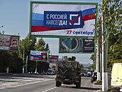 Vojenské auto projíždí pod billboardem s nápisem: „S Ruskem navždy, 27. září“,...