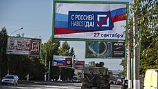 Vojenské auto projíždí pod billboardem s nápisem: „S Ruskem navždy, 27. září“,...