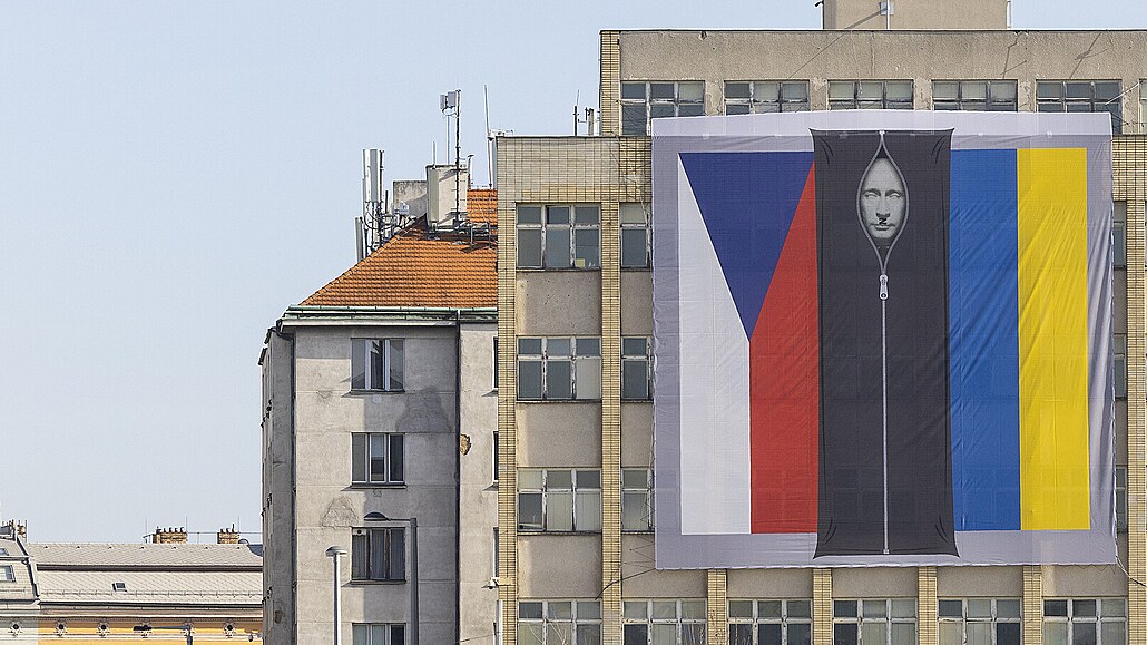 Na budov vnitra v Praze visí vlajky R a Ukrajiny s vytrácející se Putinovou...