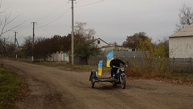 Uitel Jurij Nevoluk jede na motocyklu s nrodnmi vlajkami ve vesnici Blahodatne v Chersonsk oblasti, kterou znovu dobyla ukrajinsk armda. (11. listopadu 2022)