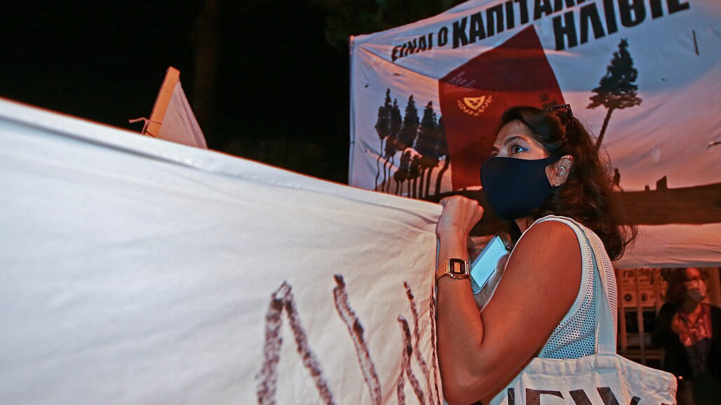 Demonstrant stojí před transparentem, který zní - v řečtině - „Je to...