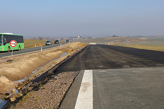 Konec stávající silnice a nové ásti s ji poloenou vrstvou asfaltu.