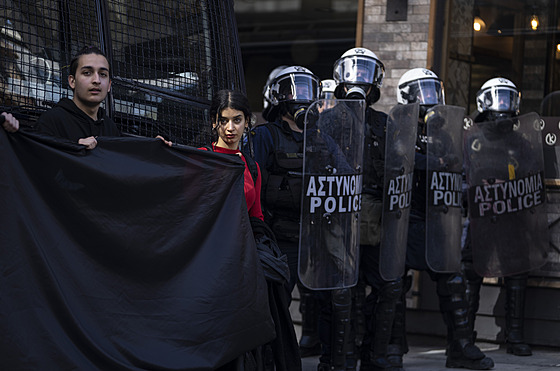 Univerzitní studenti drí erné sukno a stojí vedle policist, kteí brání...