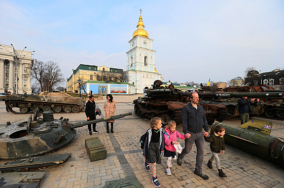 Muž s dětmi prochází kolem pouliční výstavy zničených ruských vojenských...