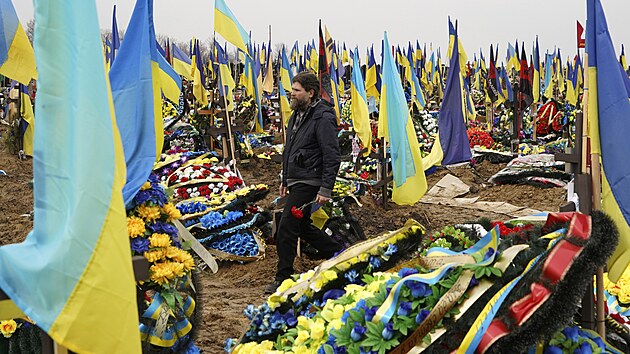 Muž nese květiny, aby je položil u hrobu zabitého vojáka na městském hřbitově v Charkově na Ukrajině. (21. března 2023)