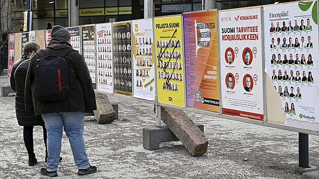 Lid prochzej kolem volebnch plakt kandidt pro parlamentn volby ve finskm Espoo. (21. bezna 2023)