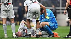 Jakub Brabec leí na trávníku, jeho stav kontrolují spoluhrái z Arisu Solu.