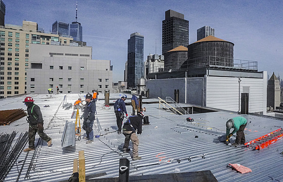 Stavební dělníci obnovují střešní krytinu výškové budovy ve finanční čtvrti na...