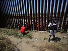 Migranti se hromadí ped plotem, který v exponovaných úsecích chrání americkou...