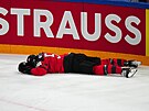 Kanadský obránce MacKenzie Weegar (52) leí na led po zákroku lotyského...