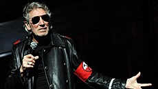 Roger Waters v černém kabátě s červenou páskou na paži.