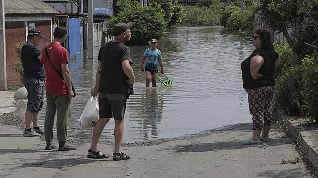 Místní obyvatelé hovoří u svých domů zaplavených vodou poté, co ruská vojska v noci vyhodila do povětří přehradu Kachovka. (6. června 2023)