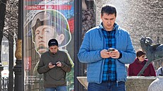 Muži hledí do svých telefonů před náborovým billboardem v Petrohradě. (12....