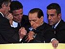 Silvio Berlusconi (druhý zprava) je podpírán na pódiu, kdy se skácel bhem...