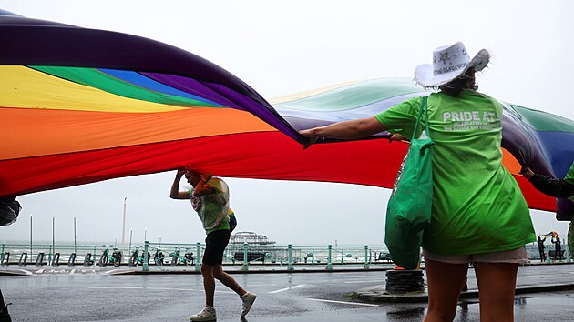 astnci pochodu Pride bojuj v nepznivm poas s duhovou vlajkou v britskm Brightonu. (5. srpna 2023)