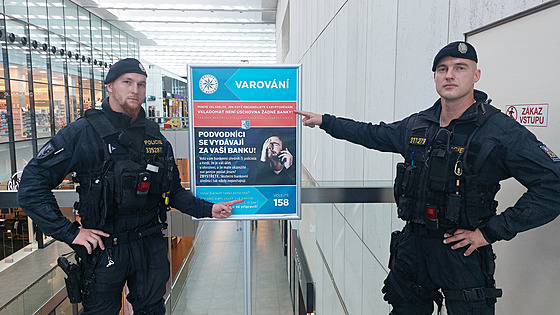 Policisté s plakátem varujícím před podvodníky vydávajícími se za bankovní...
