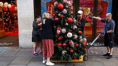 Pracovníci a zaměstnanci umísťují vánoční stromek před londýnským hračkářstvím...