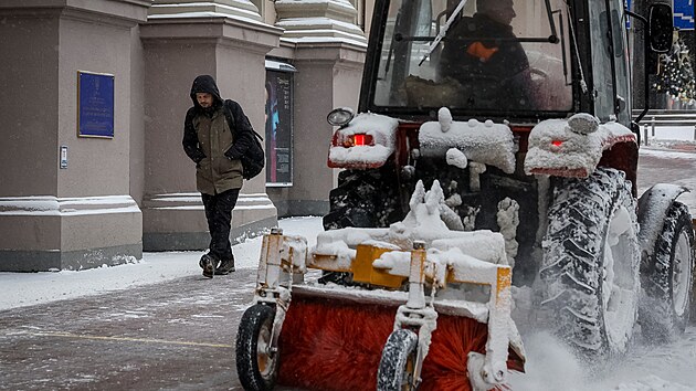 Mu� jde po ulici v Kyjev�, zat�mco sn�n� pluh odkl�z� sn�h. (27. listopadu 2023)