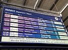 Na informaní tabuli je zobrazen seznam vlak odjídjících z nádraí...