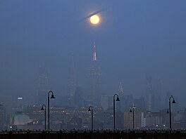 Studený Msíc v úplku vychází v mlze za panoramatem Manhattanu a Empire State...
