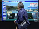 Mu prochází kolem obrazovky informující o otesech zem na ostrov Okinawa....