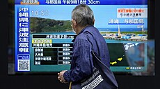 Mu prochází kolem obrazovky informující o otesech zem na ostrov Okinawa....
