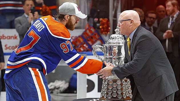 Connor McDavid (97) pebr za Edmonton Oilers trofej pro vtze Zpadn konference NHL. Gratuluje mu Bill Daly.