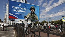 Lidé procházejí kolem billboardu s vyobrazením ruského vojáka a nápisem Hrdost...