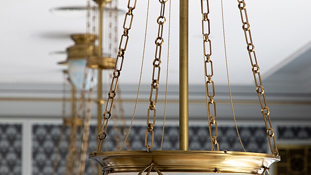 Secesn� z�v�sn� lampy se zlacen�mi detaily osv�tluj� aulu. Zdob� je tenk� girlandy, kter� se opakuj� v siln�j��m proveden� na hlavic�ch sloup�. Na chodb�ch sv�t� p�isazen� kulat� zlacen� sv�tidla a z�v�sn� b�l� koule, na schodi�ti kubistick� �pi�at�, kter� koresponduj� s lucernami na sloupc�ch.