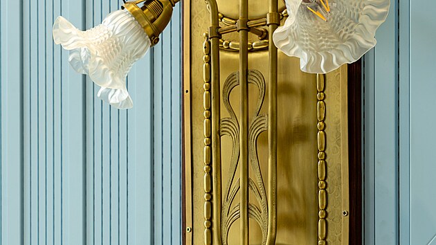 Lampy. Zlat� kv�tiny vyr�staj� ze st�n auly a v pozdn�m odpoledni ji osv�tluj� m�kk�m sv�tlem. A� jsou lampy pom�rn� velk�, sv�m secesn�m tvaroslov�m p�sob� subtiln�.