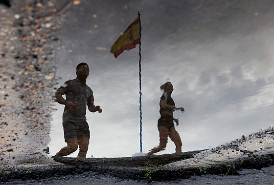 Lidé krá�ejí vedle �pan�lské vlajky s oblohou pokrytou mraky bou�e DANA. Po...