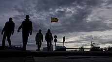 Lidé krá�ejí vedle �pan�lské vlajky s oblohou pokrytou mraky bou�e DANA. Po...