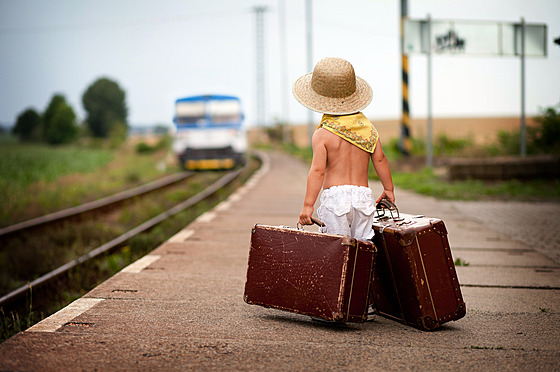 Little boy with two suitcases in hands, waiting for train on station.