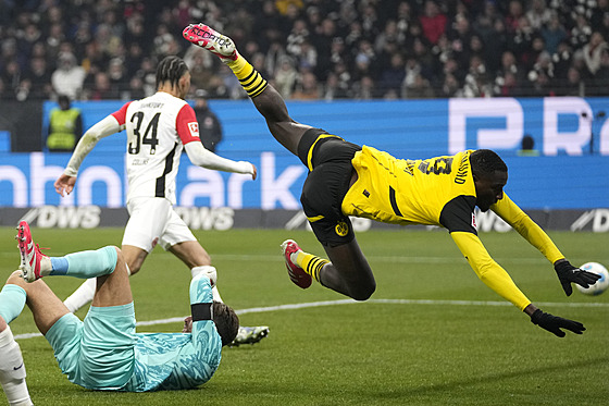 Serhou Guirassy z Dortmundu padá p�es branká�e Kevina Trappa z Frankfurtu.