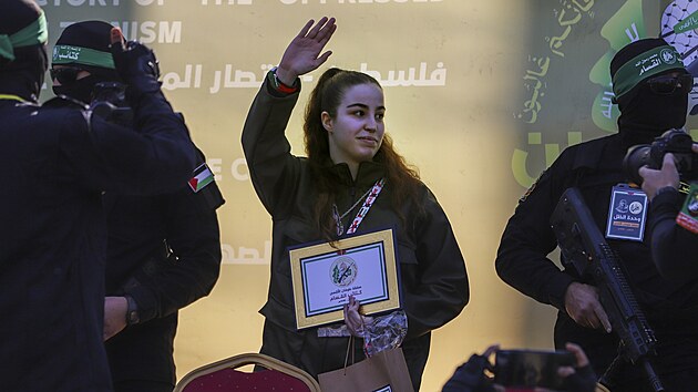 Izraelsk� voja�ka Agam Bergerov� m�v� davu vedle maskovan�ch bojovn�k� Palestinsk�ho isl�msk�ho d�ih�du, kdy� je p�ed�v�na �erven�mu k��i v uprchlick�m t�bo�e D�ab�lija v Gaze. (30. ledna 2025)