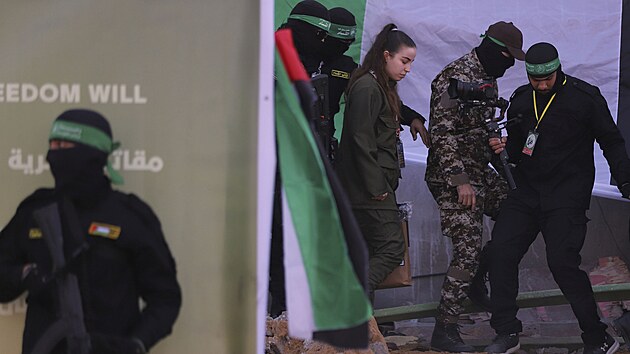 Izraelsk� voja�ka Agam Bergerov� vedle maskovan�ch bojovn�k� Palestinsk�ho isl�msk�ho d�ih�du, kdy� je p�ed�v�na �erven�mu k��i v uprchlick�m t�bo�e D�ab�lija v Gaze. (30. ledna 2025)