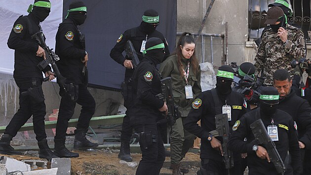 Izraelsk� voja�ka Agam Bergerov� vedle maskovan�ch bojovn�k� Palestinsk�ho isl�msk�ho d�ih�du, kdy� je p�ed�v�na �erven�mu k��i v uprchlick�m t�bo�e D�ab�lija v Gaze. (30. ledna 2025)