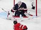 Americký branká Connor Hellebuyck zasahuje proti Samu Bennettovi.