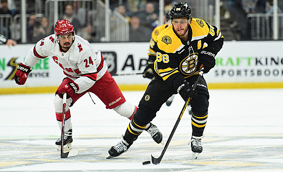 David Pastrák z Bostonu vyváí puk, sleduje ho Seth Jarvis z Caroliny.