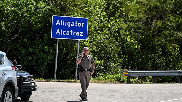 Americk� policista stoj� p�ed cedul� nav�d�j�c� k floridsk�mu deten�n�mu centru pro migranty zn�m�mu jako �Alig�to�� Alcatraz�. (22. �ervence 2025)