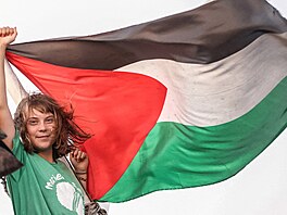 Greta Thunbergová gestikuluje vedle palestinské vlajky na lodi, která je...