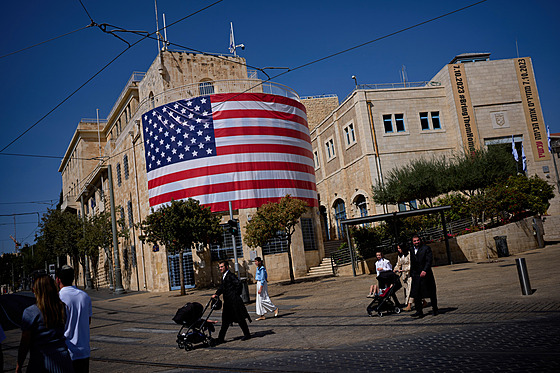 Lidé procházejí kolem velké americké vlajky zdobící budovu v centru Jeruzaléma....