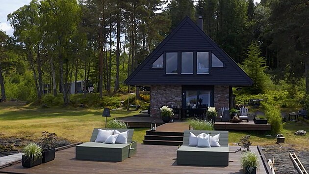 Chata po promn: exterir chaty je naten tlumenou ernou barvou, kter je Halvorovou oblbenou. Molo a terasa jsou propojeny prkny jako mdn molo.